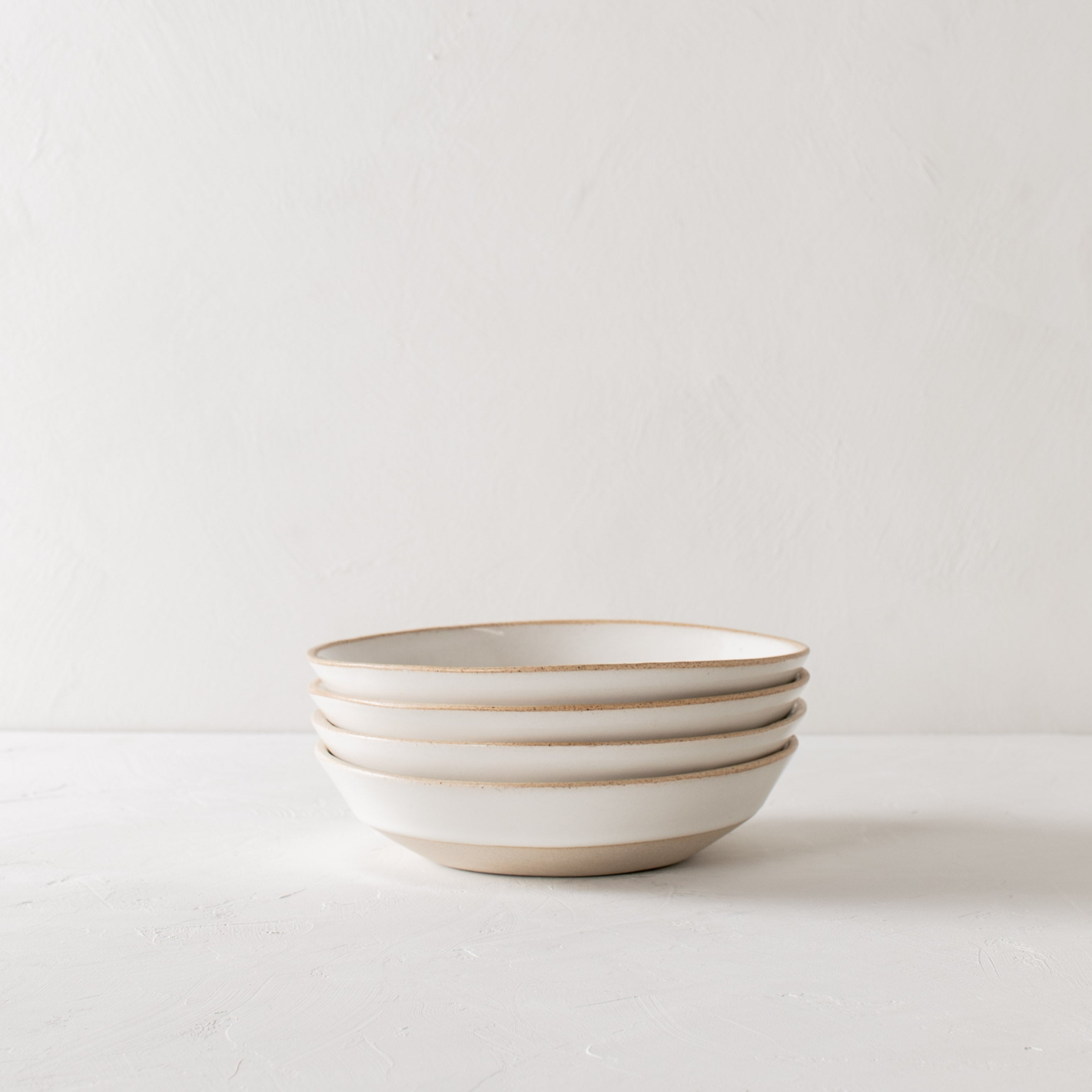 Stack of four minimal white ceramic minimal pasta bowls. Bowls have an exposed stoneware rime and base. Handmade pasta bowl designed and sold by Convivial Production, Kansas City ceramics.