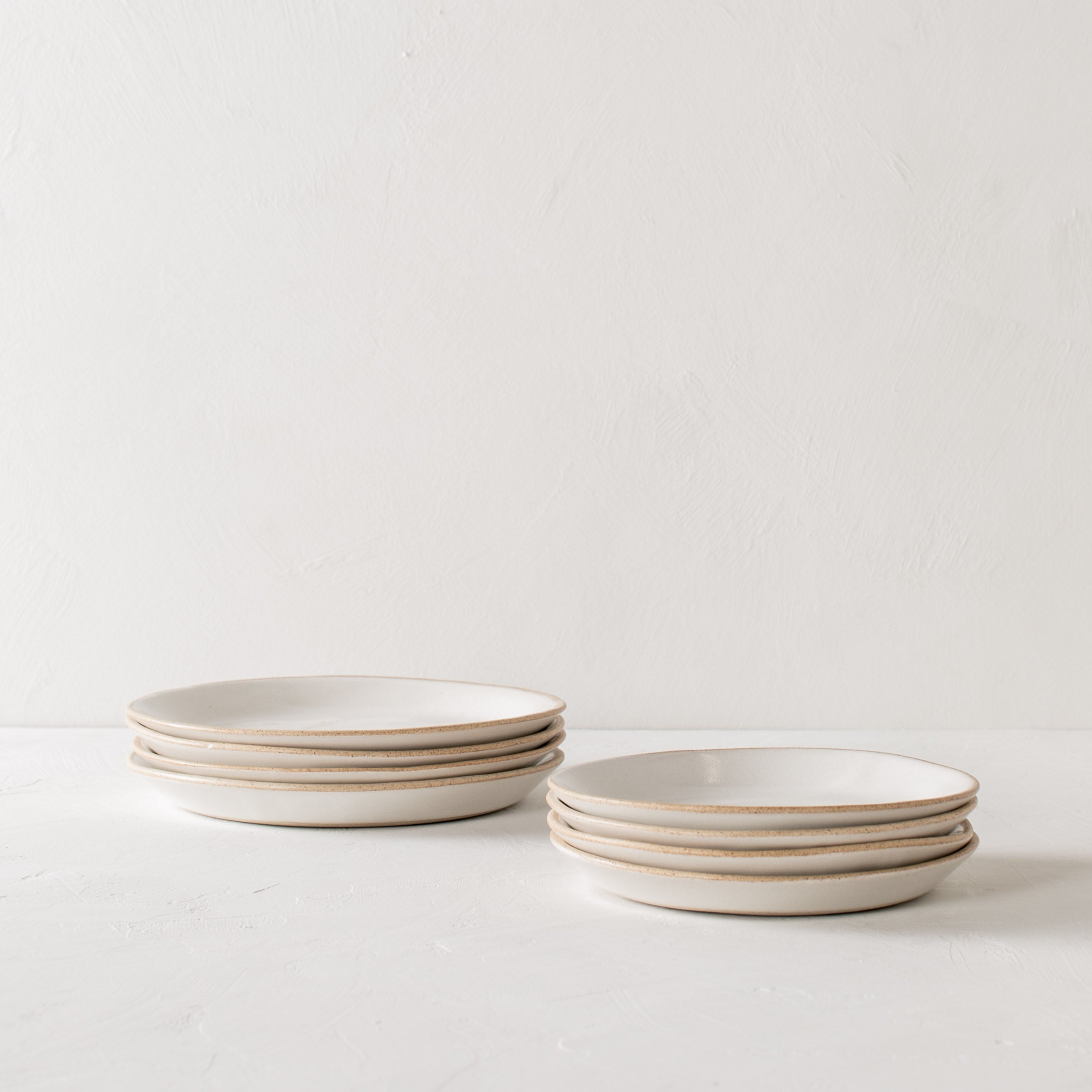 Minimal white ceramic plates stacked, four salad plates stacked beside four dinner plates. Handmade ceramic plates, designed and sold by Convivial Production, Kansas City ceramics.