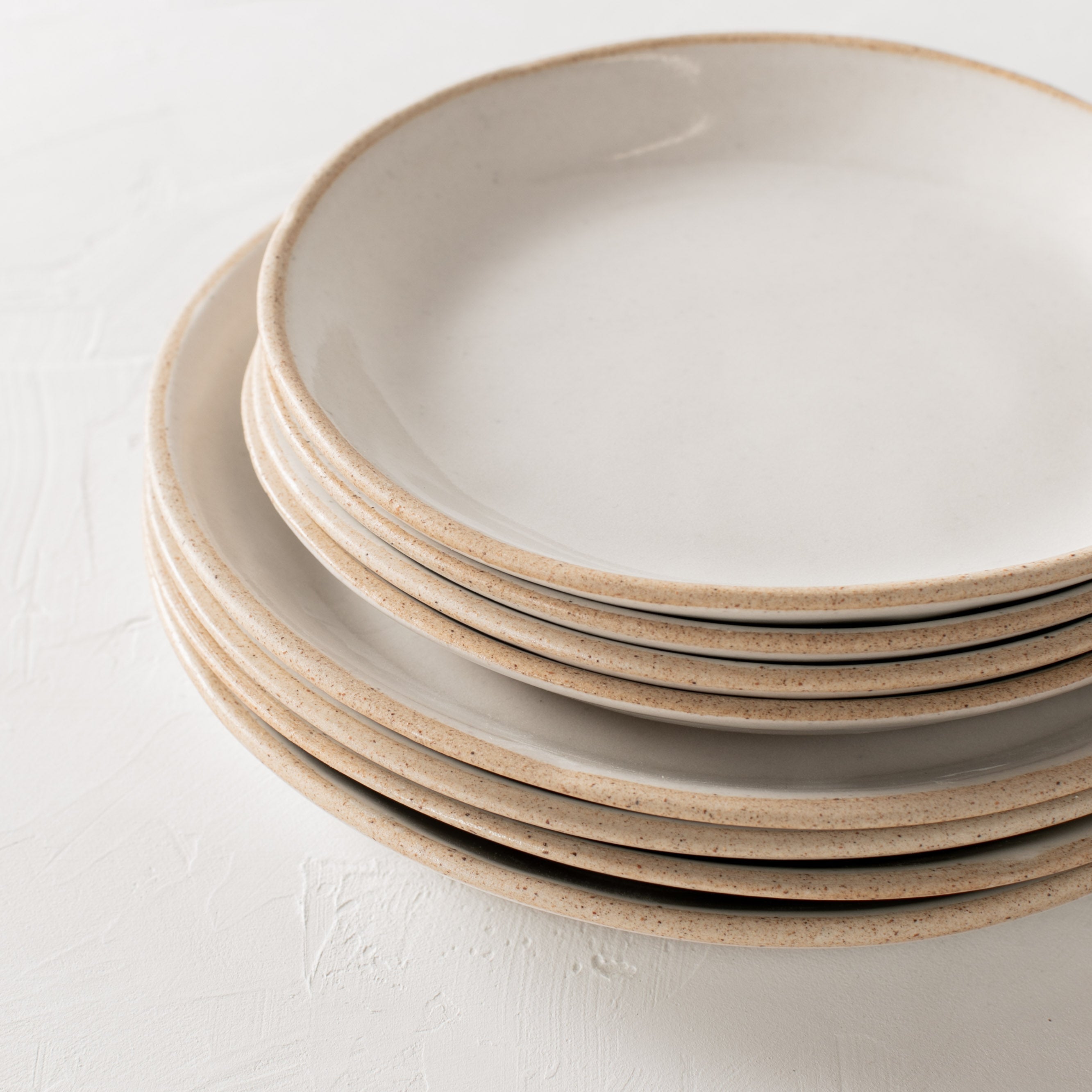 Minimal white ceramic plates stacked, closeup of four salad plates stacked on four dinner plates. Handmade ceramic plates, designed and sold by Convivial Production, Kansas City ceramics.