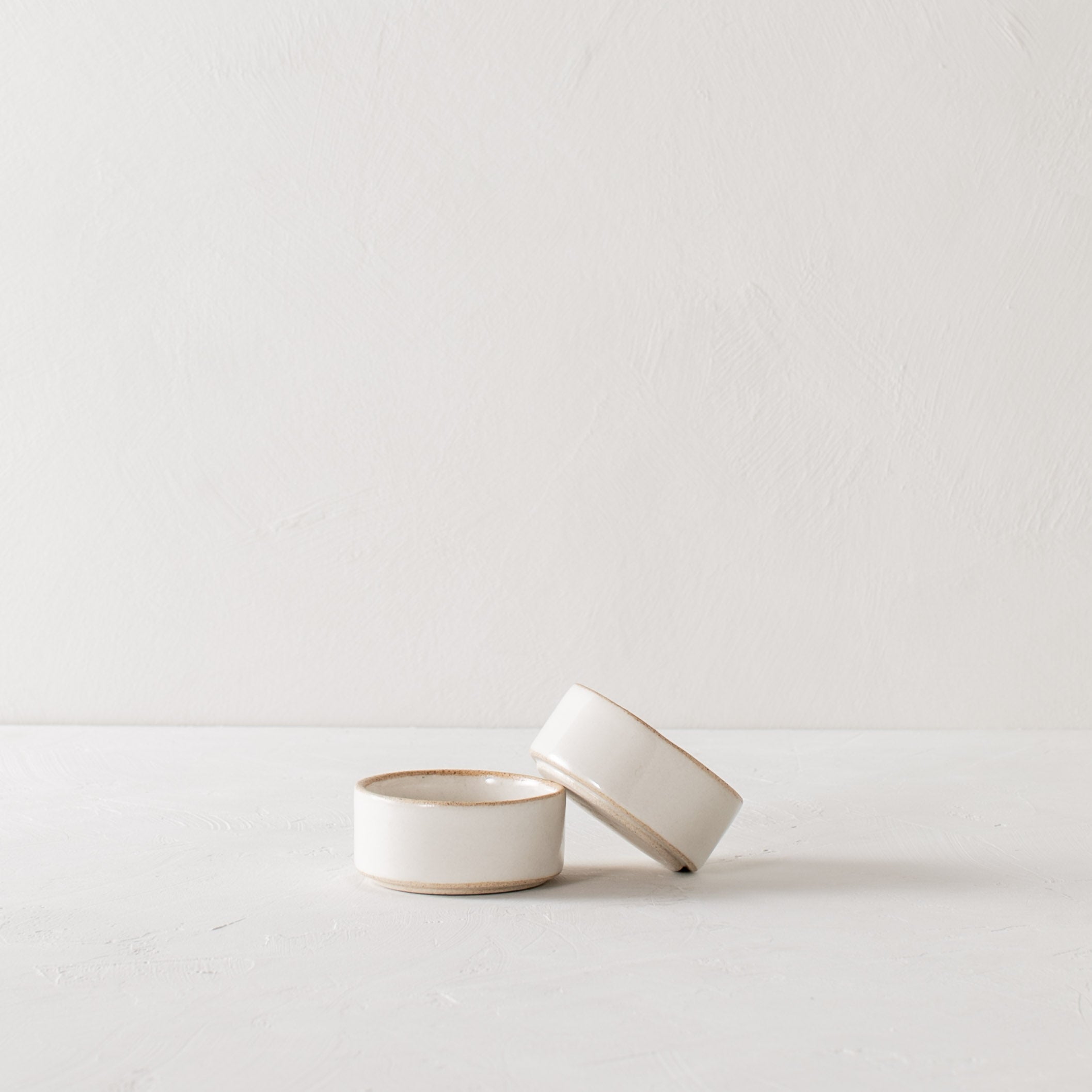 Pair of two white ceramic ramekins with exposed stoneware rims and bases. One ramekin leaning on the other. Handmade ceramic ramekins, designed and sold by Convivial Production, Kansas City ceramics.   
