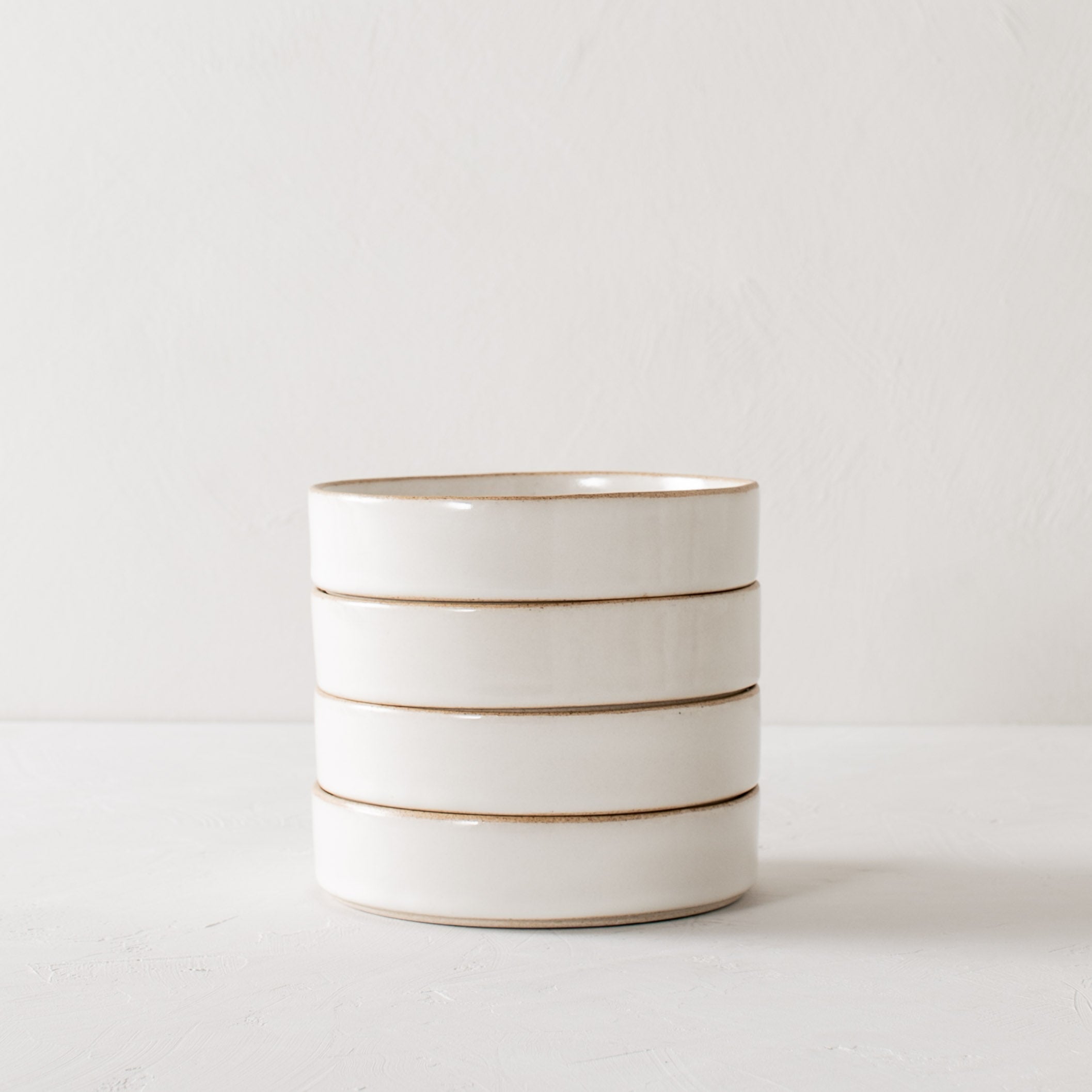 Stack of four minimal white ceramic minimal salad dishes. Dishes have exposed stoneware rims and bases. Handmade salad dishes, designed and sold by Convivial Production, Kansas City ceramics.