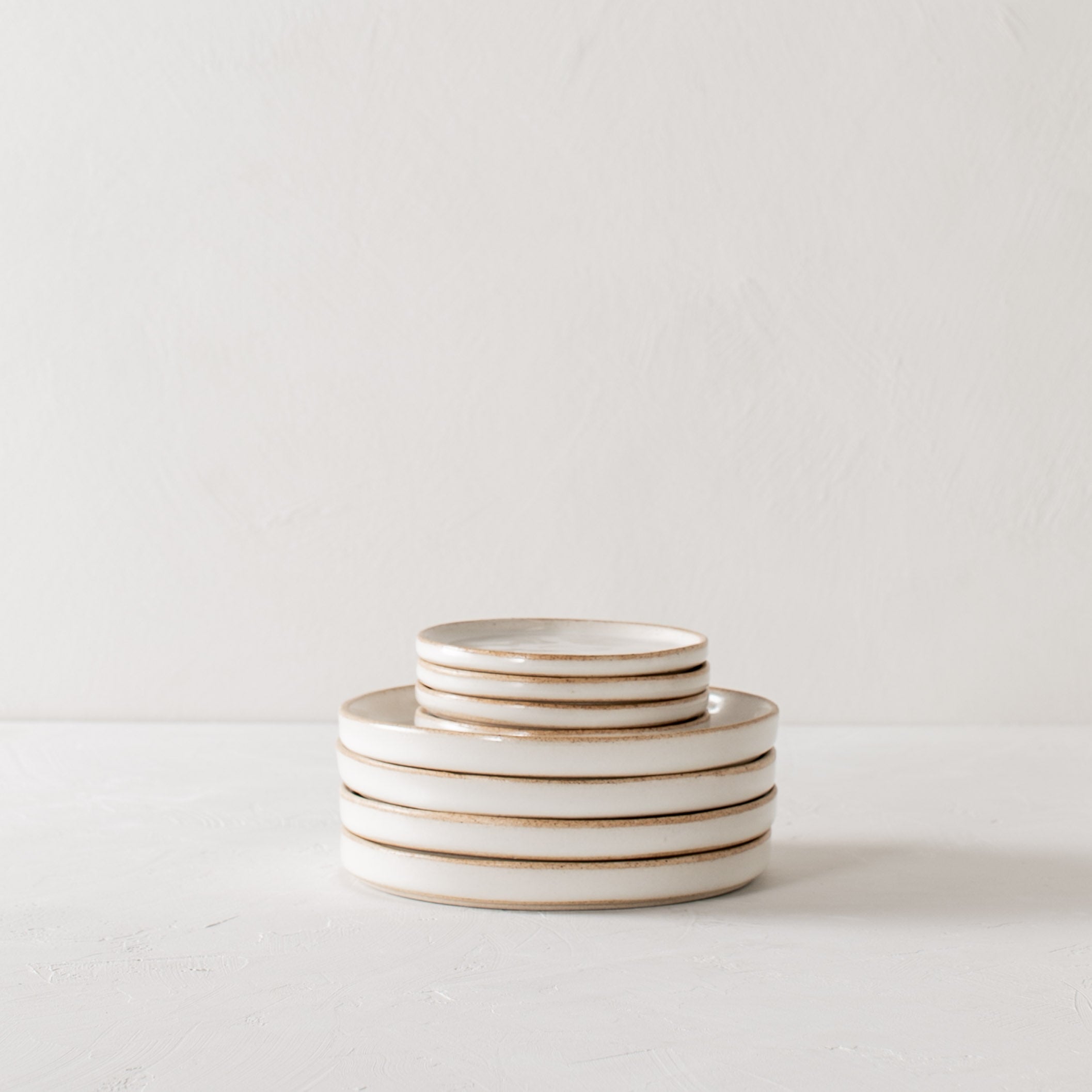 Stack of four ceramic 4 inch side dishes atop a stack of four 6 inch side. Dishes have exposed stoneware rims and bases. Handmade ceramic side dishes designed and sold by Convivial Production, Kansas City ceramics.
