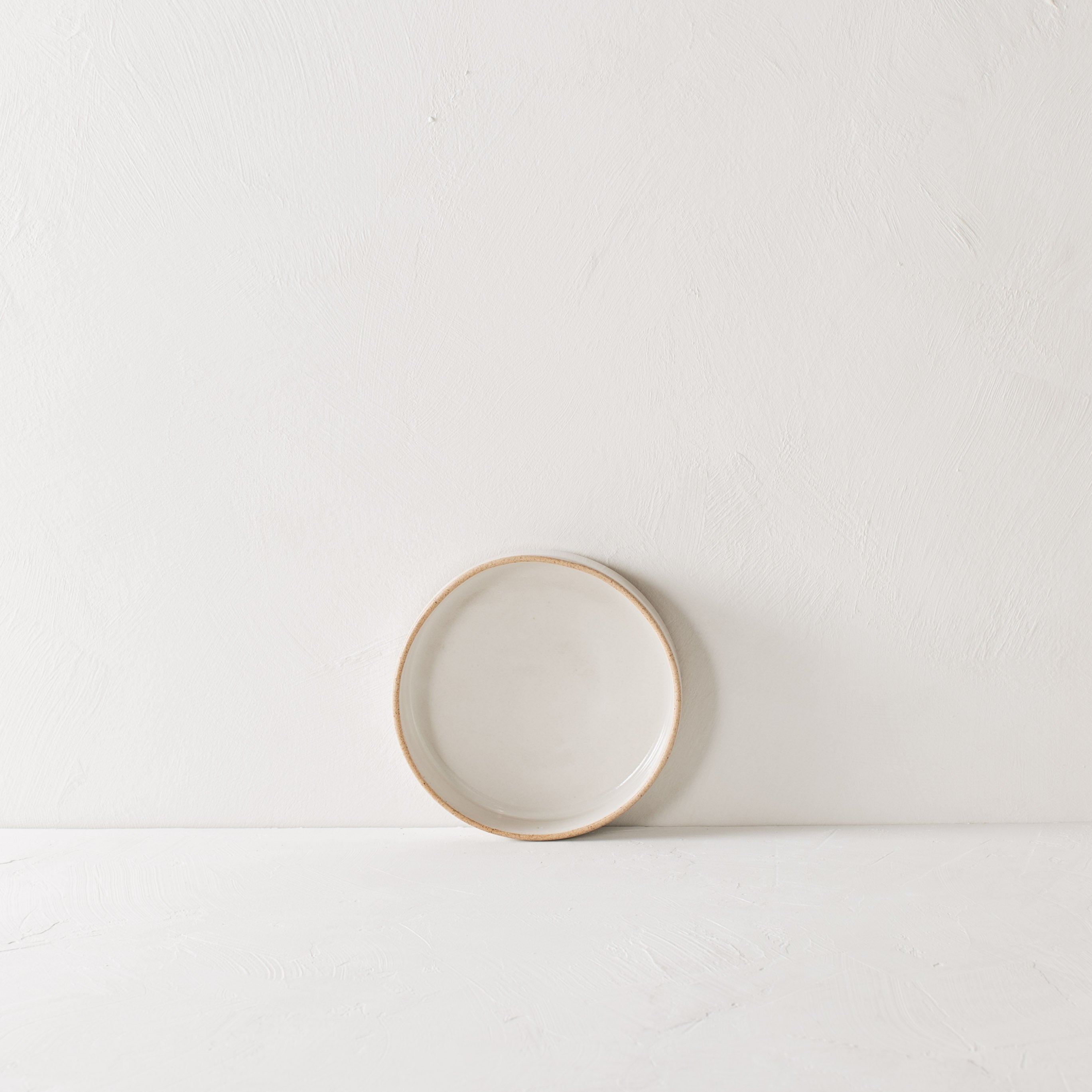 Minimal white salad dish leaning against the backdrop. Exposed stoneware rim can be seen. Handmade ceramic salad dish, designed and sold by Convivial Production, Kansas City ceramics.