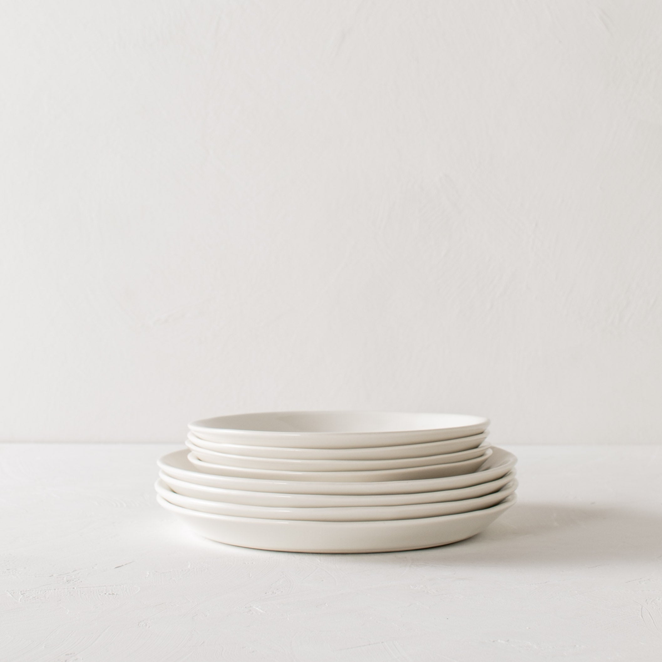 Stack of dinner plates and salad plates. Four salad plates on top of four dinner plates. Backdrops is a white plaster backdrop and white plaster textured tabletop. Handmade ceramic plates designed and sold by Convivial Production, Kansas City ceramics.