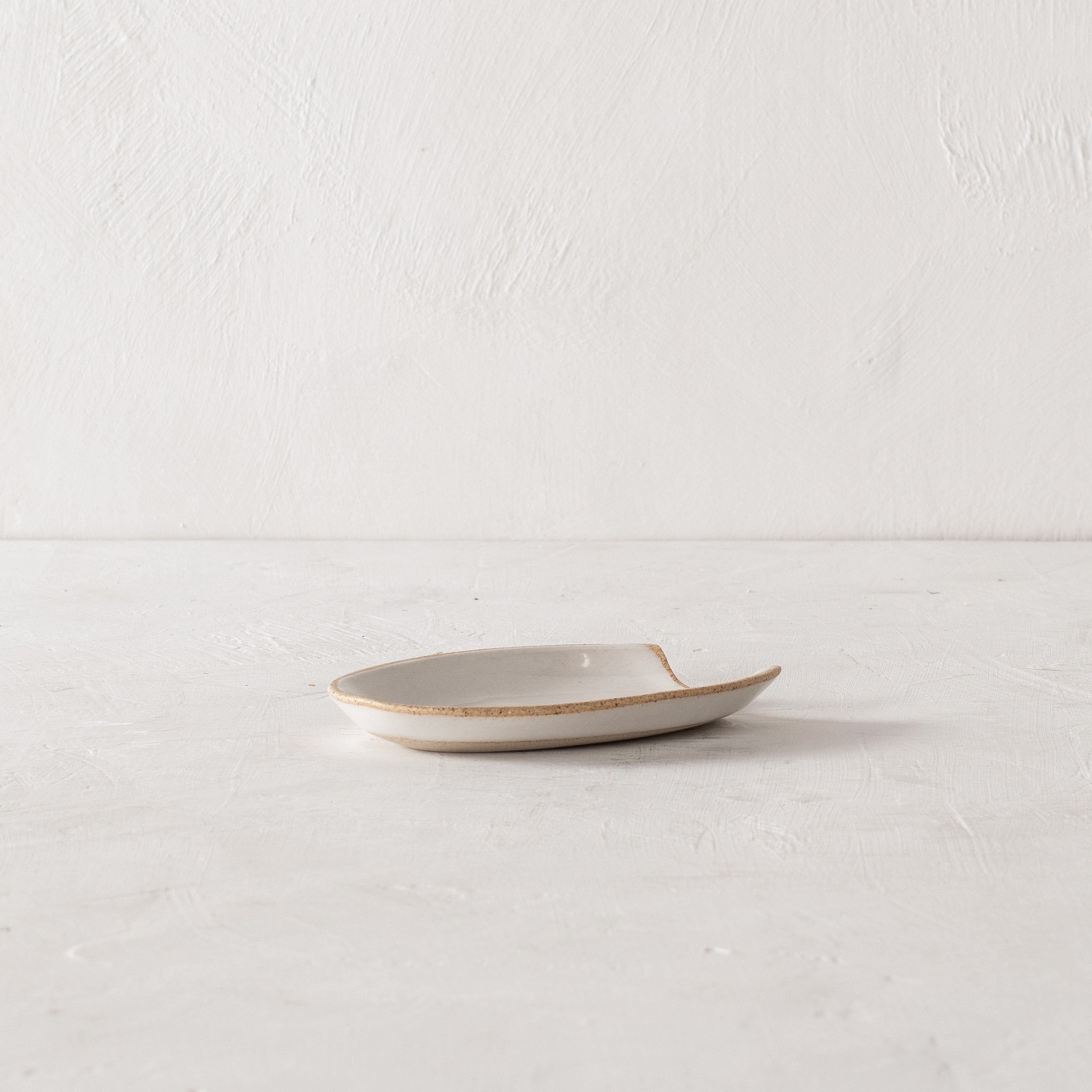 Arch shaped spoon rest with a white glaze over stoneware. The spoon rest's rim is an exposed stoneware. Handmade ceramic spoon rest designed and sold by Convivial Production, Kansas City ceramics.