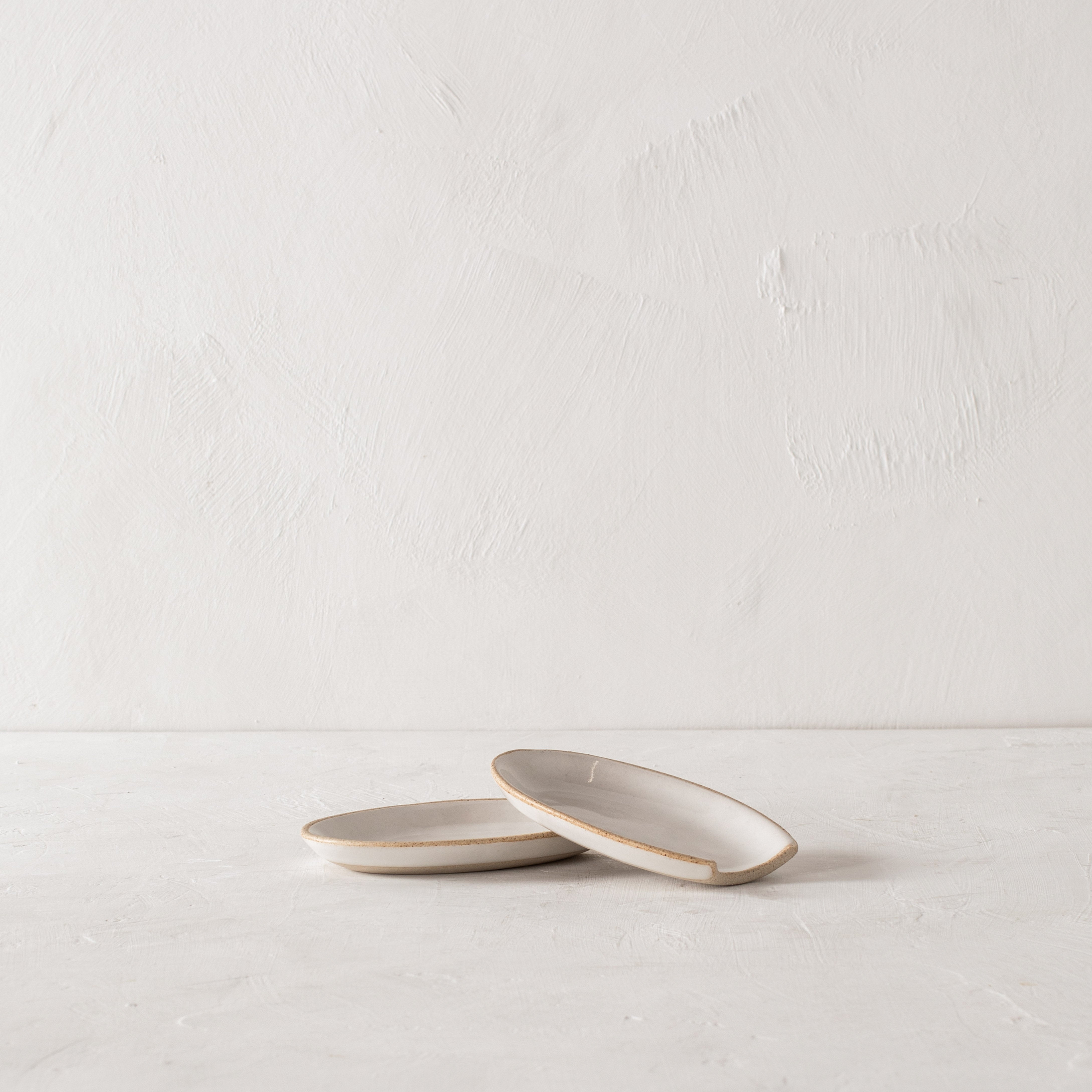 White ceramic spoon rests stacked on top of each other. Spoon rest is in an oval shape with an exposed stoneware rim. Hand made ceramic spoon rest sold and designed by Convivial Production, Kansas City ceramics.