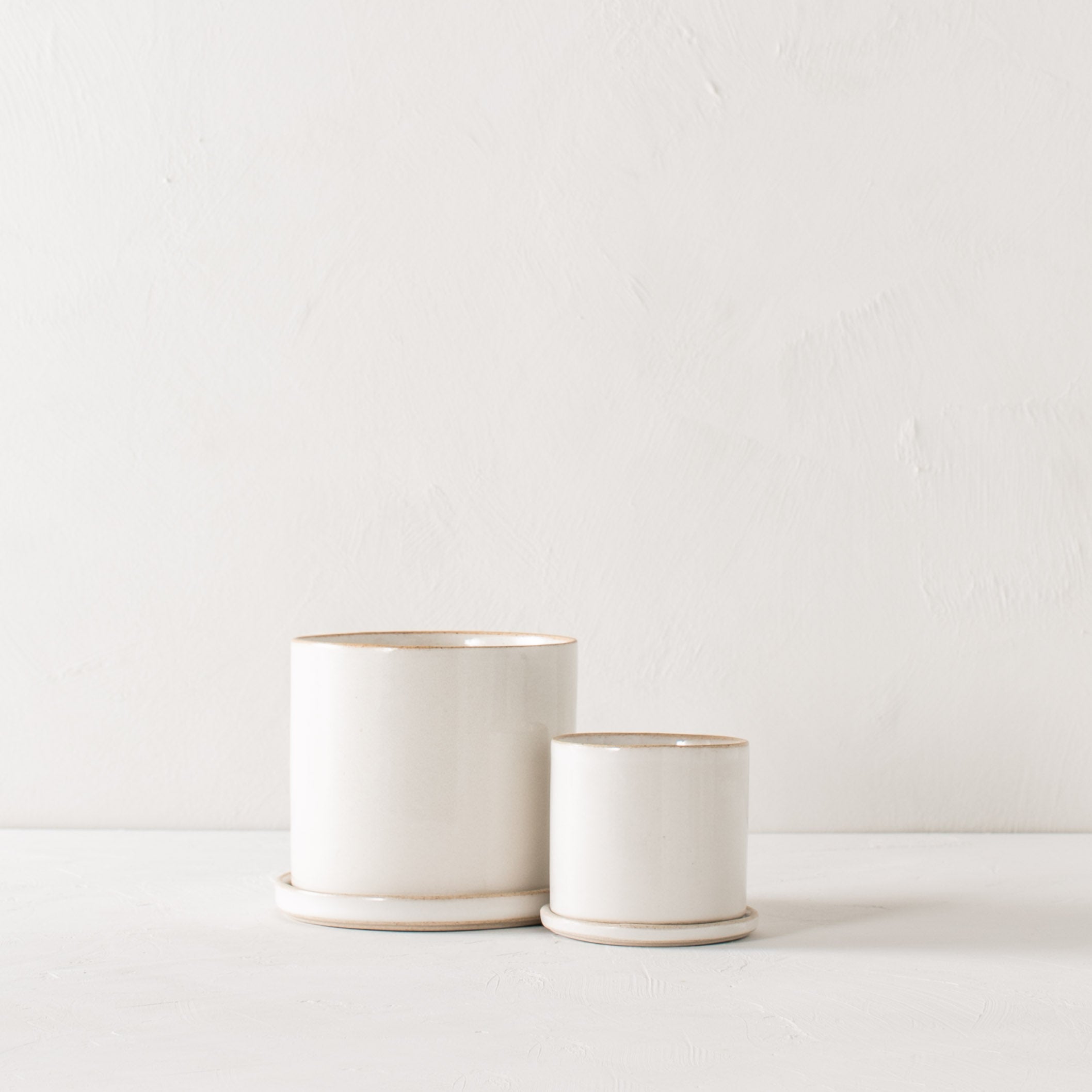 Two minimal white ceramic planters, they have exposed stoneware rims and bases. Both have bottom drainage dishes. Handmade ceramic planters designed and sold by Convivial Production, Kansas City ceramics. 