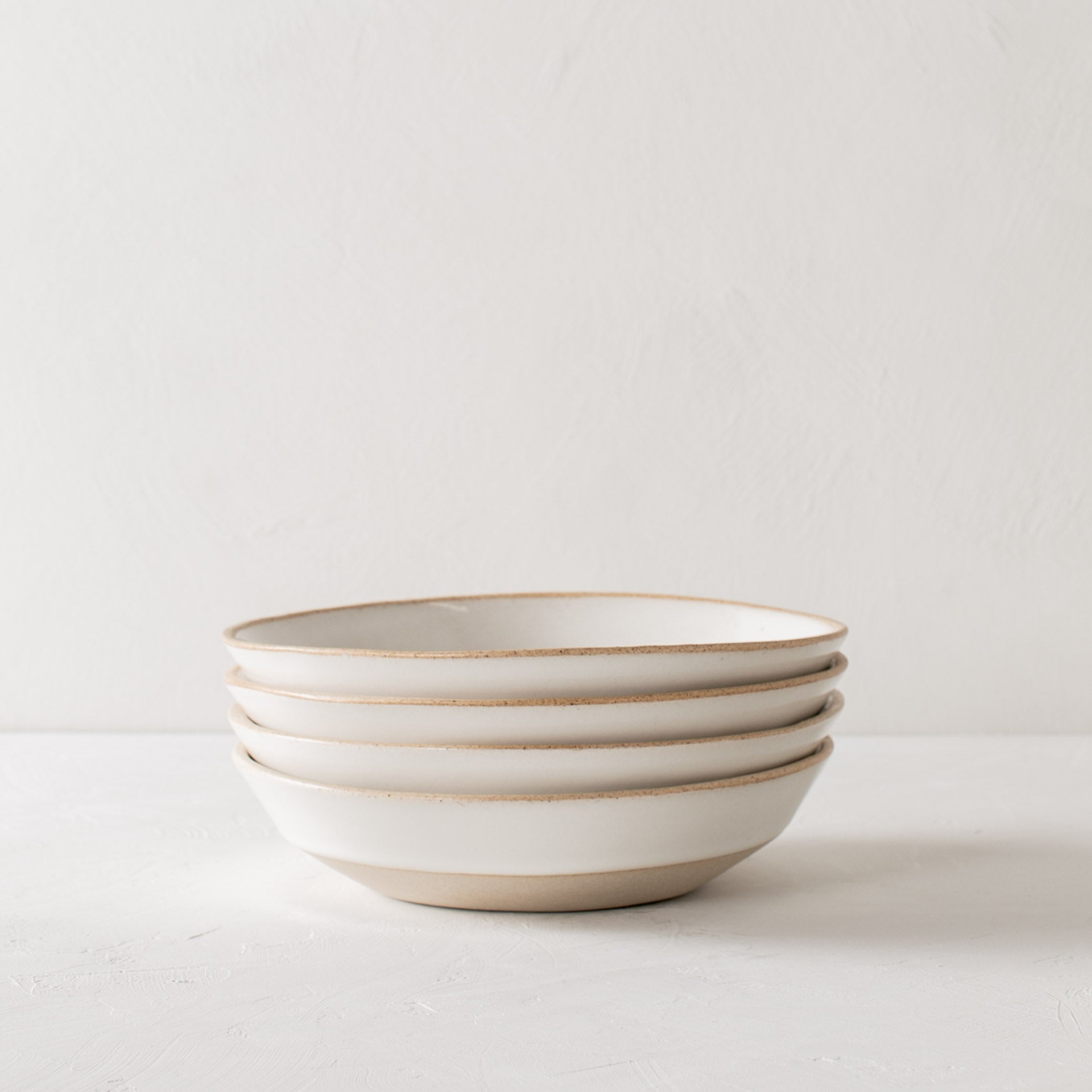 Stack of four minimal white ceramic minimal pasta bowls. Bowls have an exposed stoneware rime and base. Handmade pasta bowl designed and sold by Convivial Production, Kansas City ceramics.