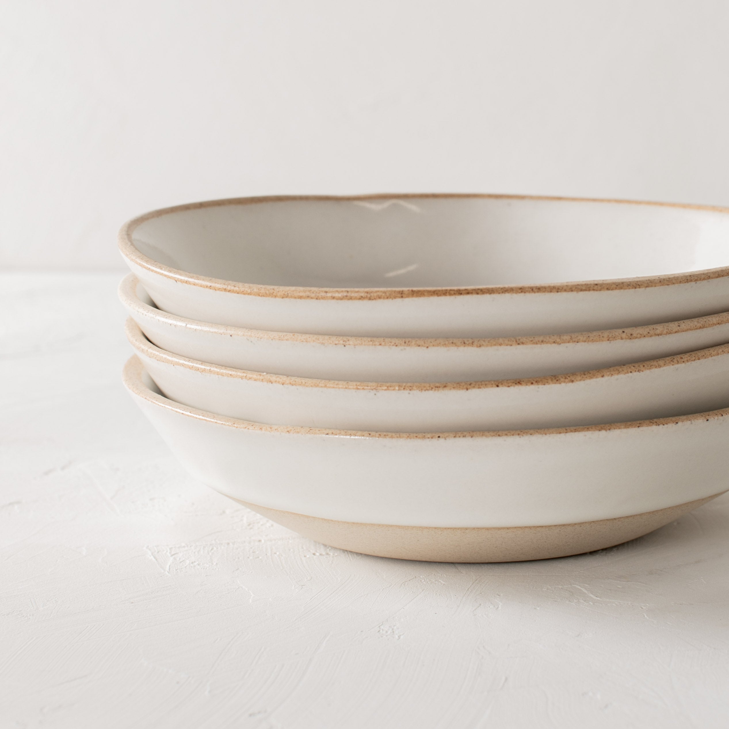 Stack of four minimal white ceramic minimal pasta bowls, close up image. Bowls have an exposed stoneware rime and base. Handmade pasta bowl designed and sold by Convivial Production, Kansas City ceramics.