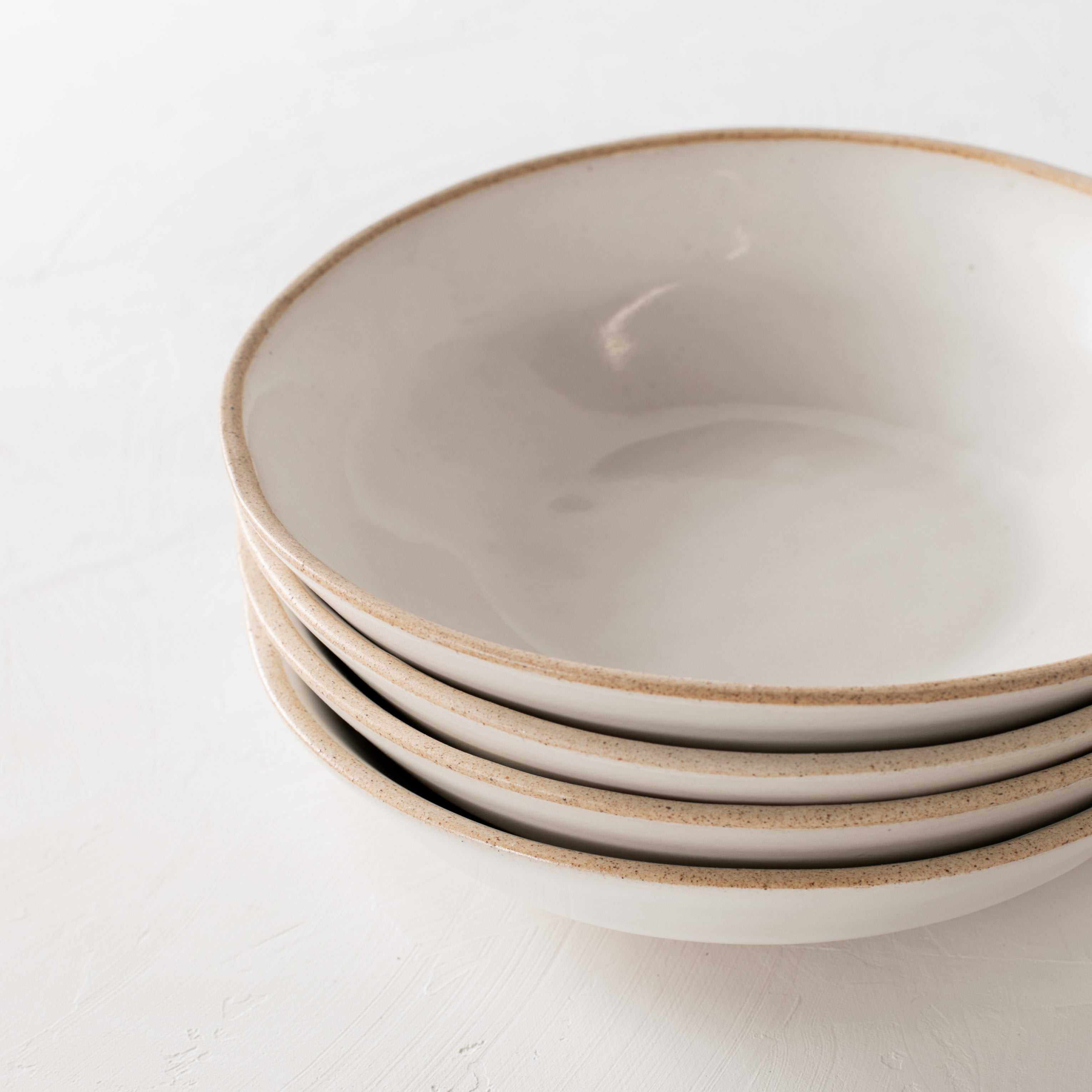 Stack of four minimal white ceramic minimal pasta bowls, close up image. Bowls have an exposed stoneware rime and base. Handmade pasta bowl designed and sold by Convivial Production, Kansas City ceramics.